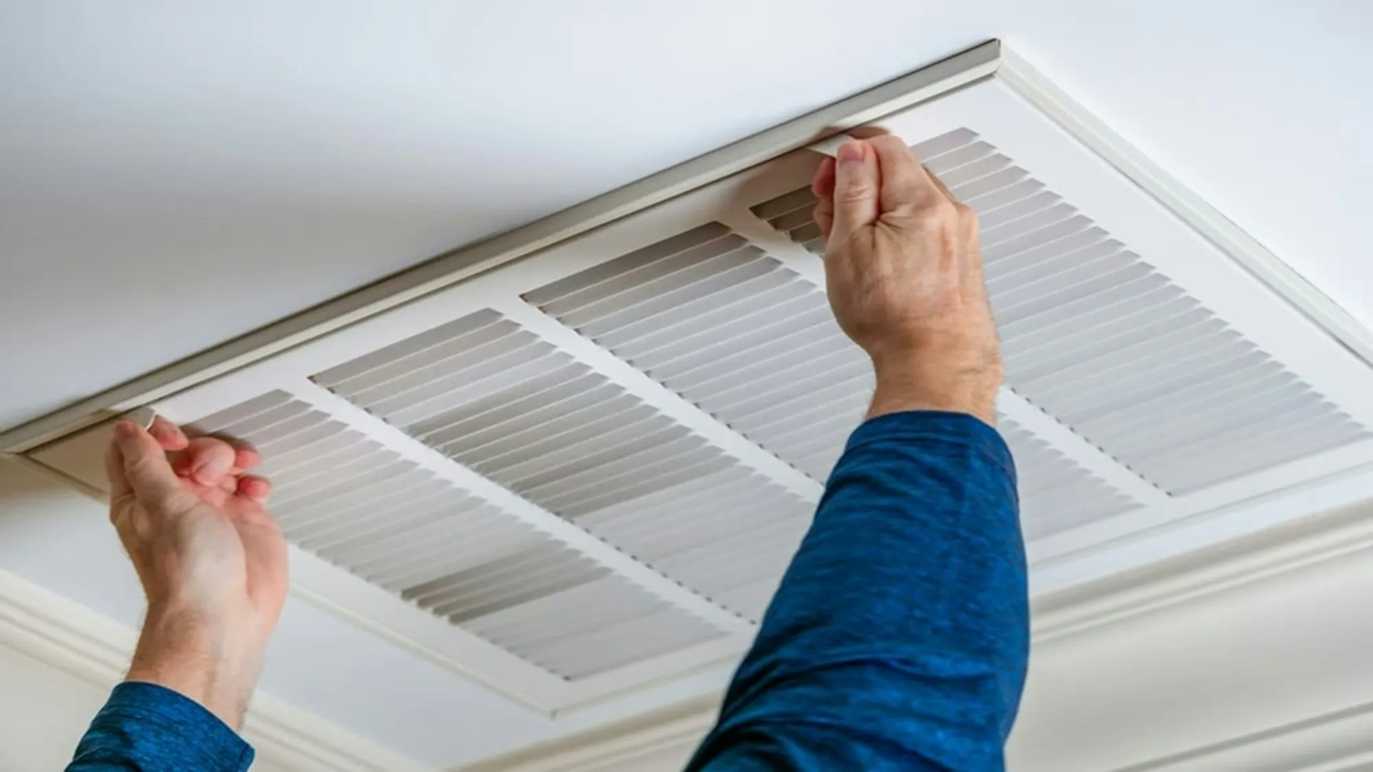 Hands fitting a white return air grille in a ceiling
